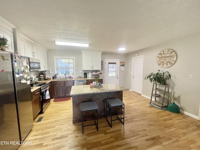 kitchen featuring a breakfast bar area, light wood-style flooring, a sink, white cabinetry, and appliances with stainless steel finishes