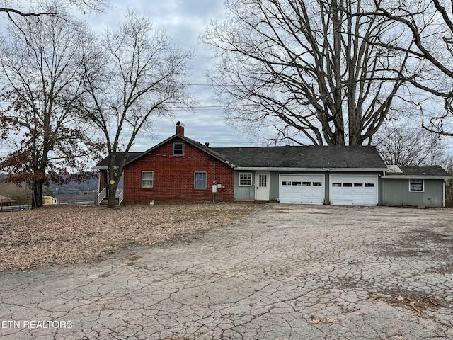 view of side of home with an attached garage, driveway, a chimney, and brick siding