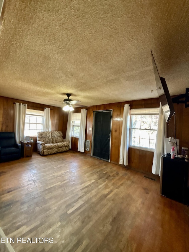 unfurnished living room featuring a ceiling fan, wood walls, and wood finished floors