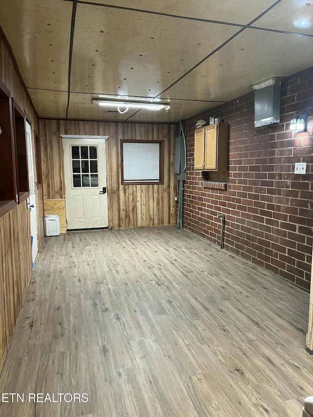 finished basement with light wood-style floors, brick wall, and wood walls