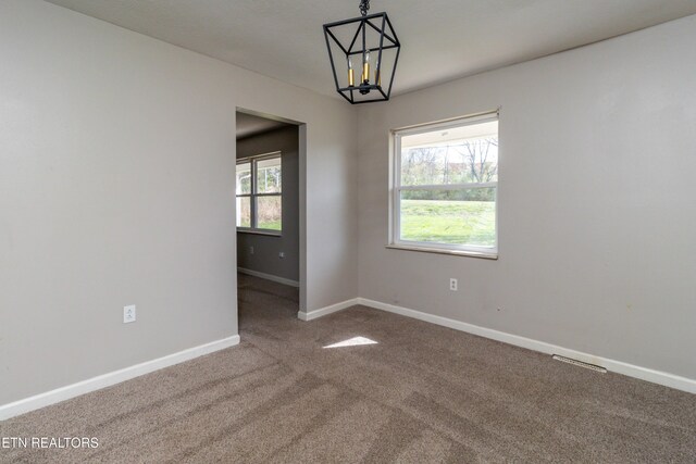 carpeted spare room with a notable chandelier, visible vents, and baseboards