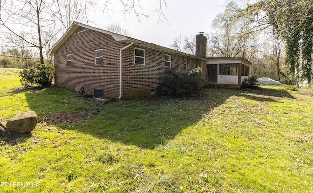 back of house with a lawn, brick siding, a sunroom, and a chimney