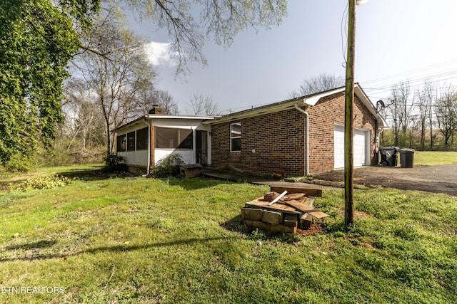 view of home's exterior with aphalt driveway, a garage, a yard, and a sunroom