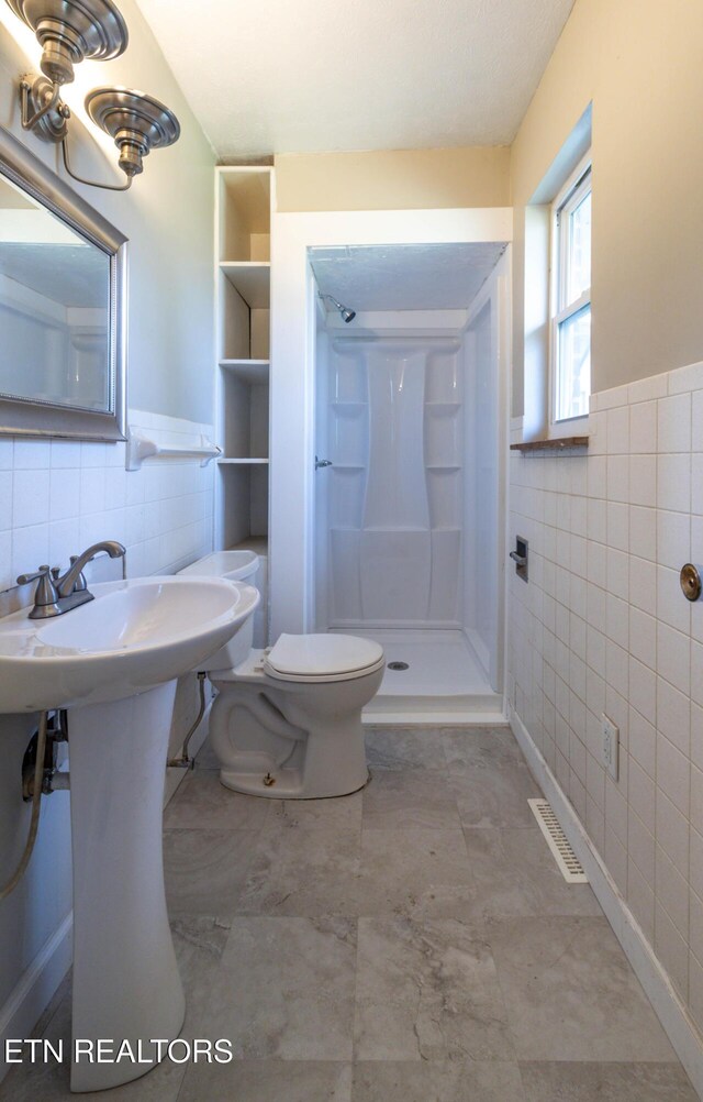 full bath with toilet, a sink, tile walls, wainscoting, and a shower stall