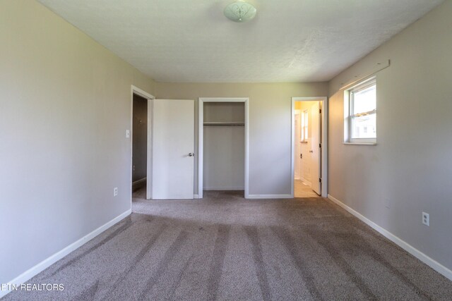 unfurnished bedroom with a closet, carpet flooring, ensuite bath, and baseboards