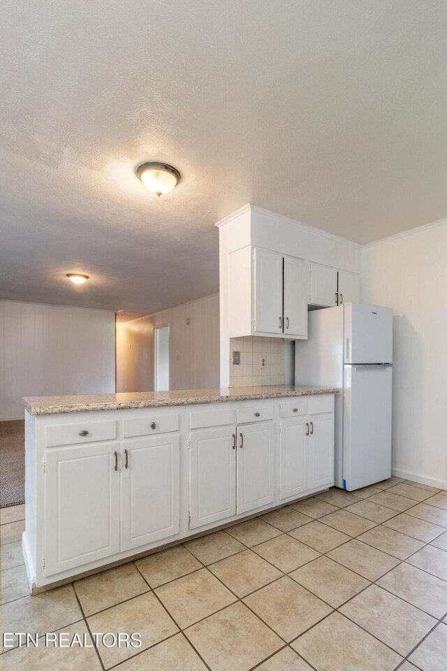 kitchen with decorative backsplash, white cabinets, light tile patterned flooring, and freestanding refrigerator