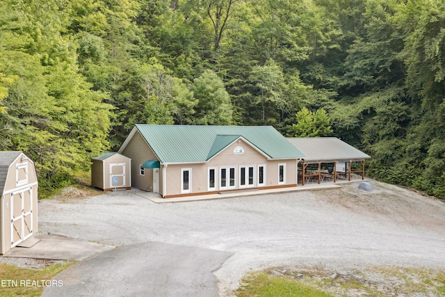 exterior space featuring an outdoor structure, a view of trees, metal roof, dirt driveway, and a shed