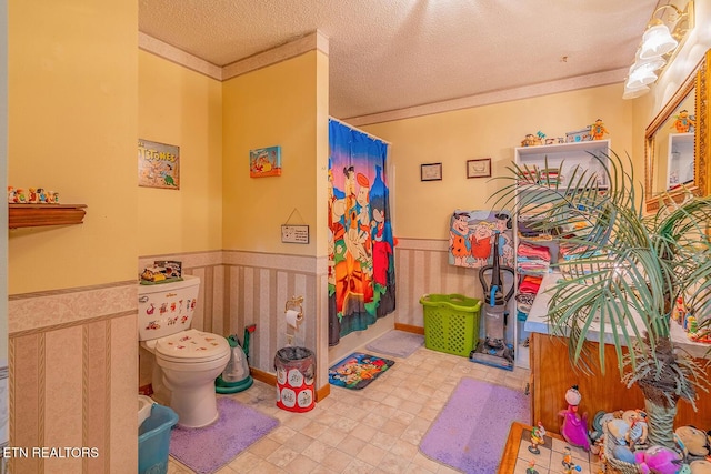 bathroom featuring wainscoting, toilet, tile patterned floors, crown molding, and a textured ceiling