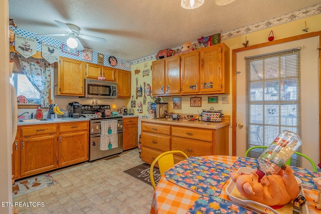 kitchen with a textured ceiling, ceiling fan, stainless steel appliances, light countertops, and light floors