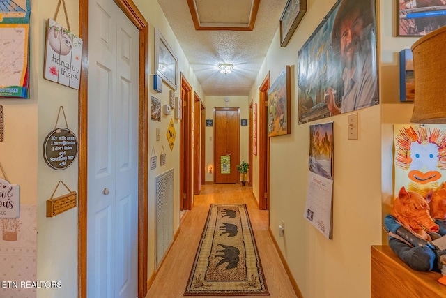 hallway with a textured ceiling, visible vents, and light wood-style floors