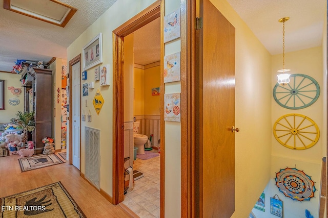 hallway featuring light wood finished floors, attic access, visible vents, and a textured ceiling