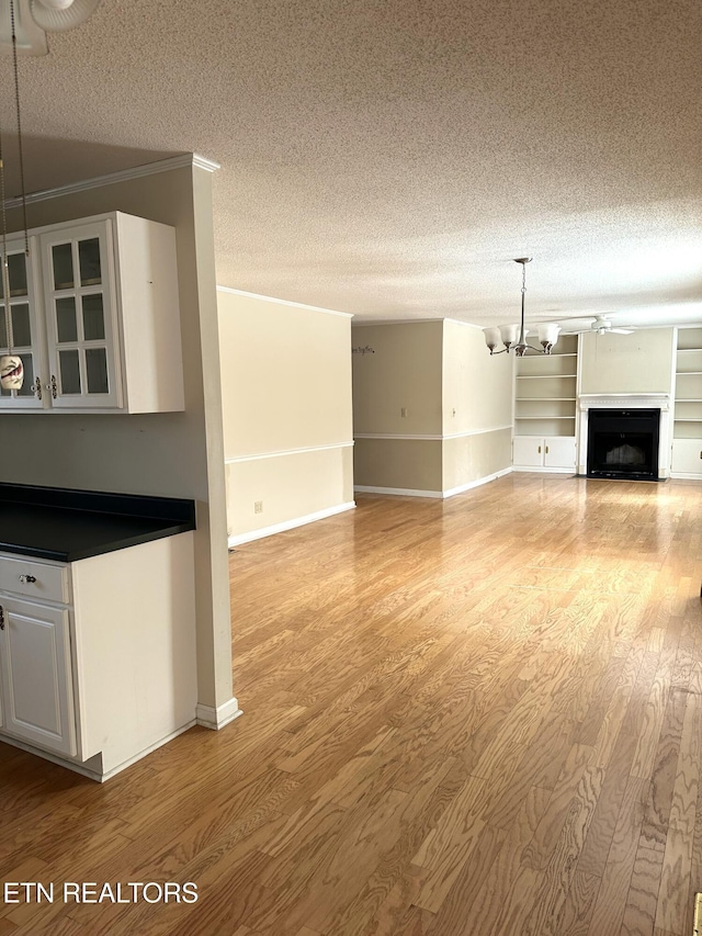 unfurnished living room featuring a textured ceiling, light wood finished floors, a fireplace, and a notable chandelier