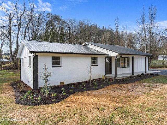 view of front facade with metal roof, a porch, brick siding, crawl space, and a front yard