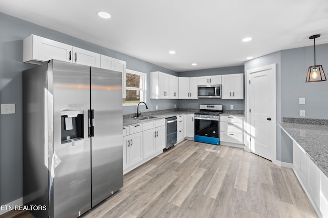 kitchen with light stone counters, decorative light fixtures, stainless steel appliances, white cabinetry, and a sink