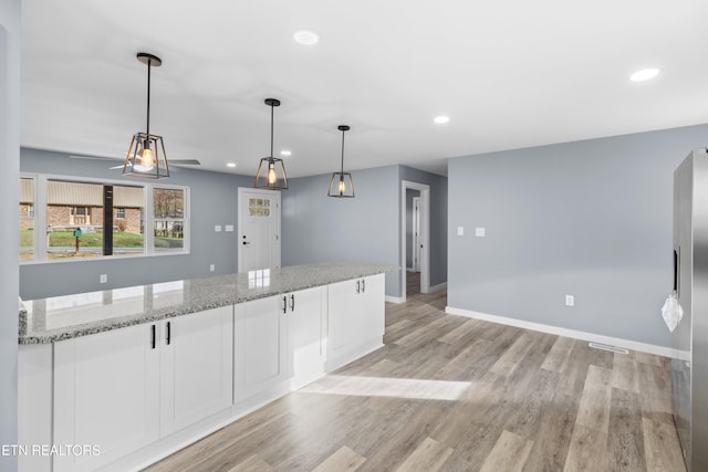 kitchen featuring hanging light fixtures, light wood-style flooring, white cabinets, light stone countertops, and baseboards