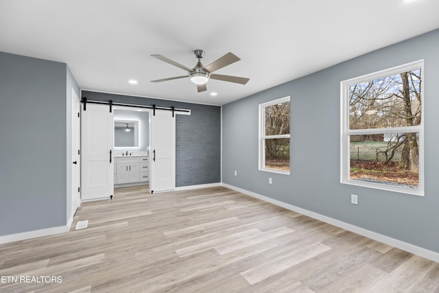 unfurnished bedroom featuring light wood-style flooring, baseboards, and a barn door