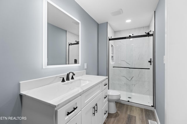 bathroom featuring toilet, a marble finish shower, wood finished floors, and vanity