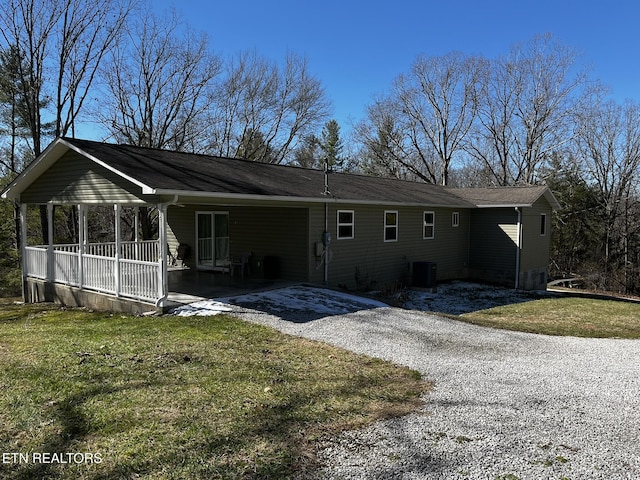 view of front of house with gravel driveway, covered porch, a front lawn, and central AC