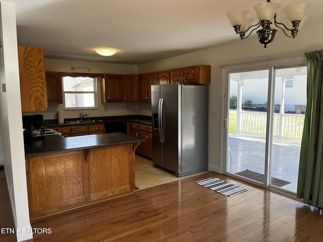 kitchen featuring stainless steel fridge, dark countertops, brown cabinets, a peninsula, and a sink