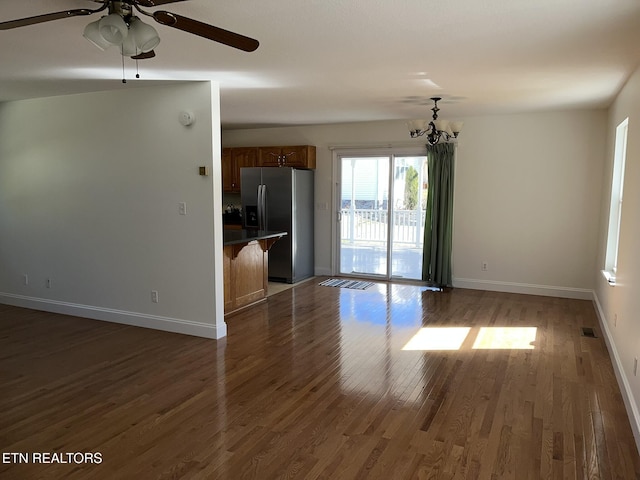 unfurnished living room featuring ceiling fan with notable chandelier, dark wood-style flooring, and baseboards