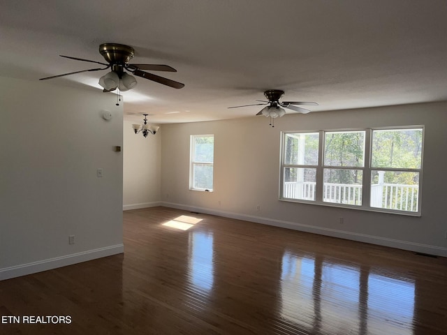 unfurnished room featuring dark wood-style floors, visible vents, baseboards, and ceiling fan with notable chandelier