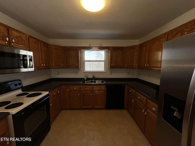 kitchen with appliances with stainless steel finishes, dark countertops, a sink, and brown cabinets