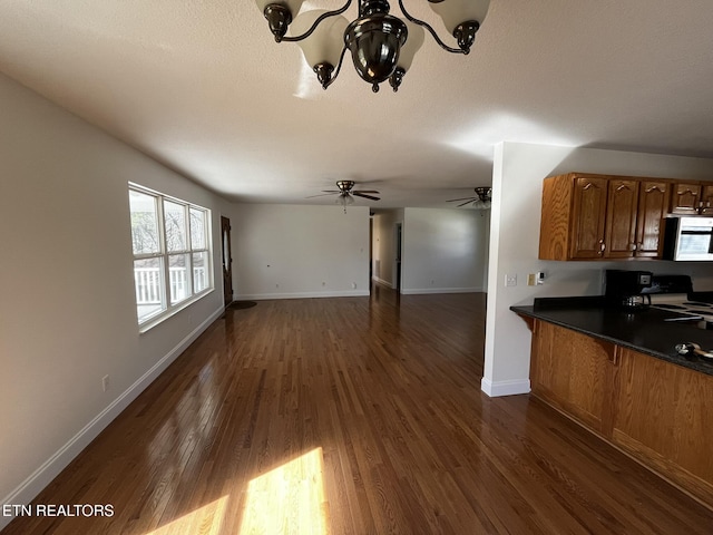 kitchen featuring baseboards, open floor plan, brown cabinets, dark countertops, and dark wood finished floors