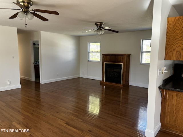 unfurnished living room with ceiling fan, a fireplace, dark wood finished floors, and baseboards