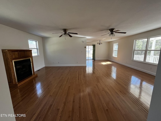 unfurnished living room with ceiling fan, baseboards, a fireplace with raised hearth, and dark wood-style flooring