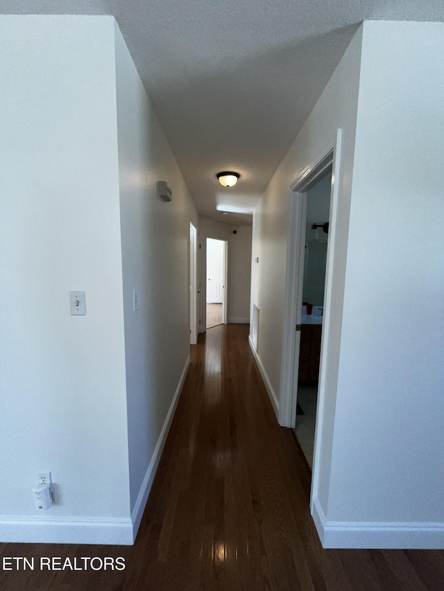 corridor featuring baseboards and dark wood finished floors