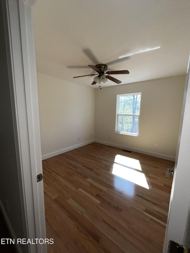 unfurnished room with dark wood-type flooring, visible vents, ceiling fan, and baseboards