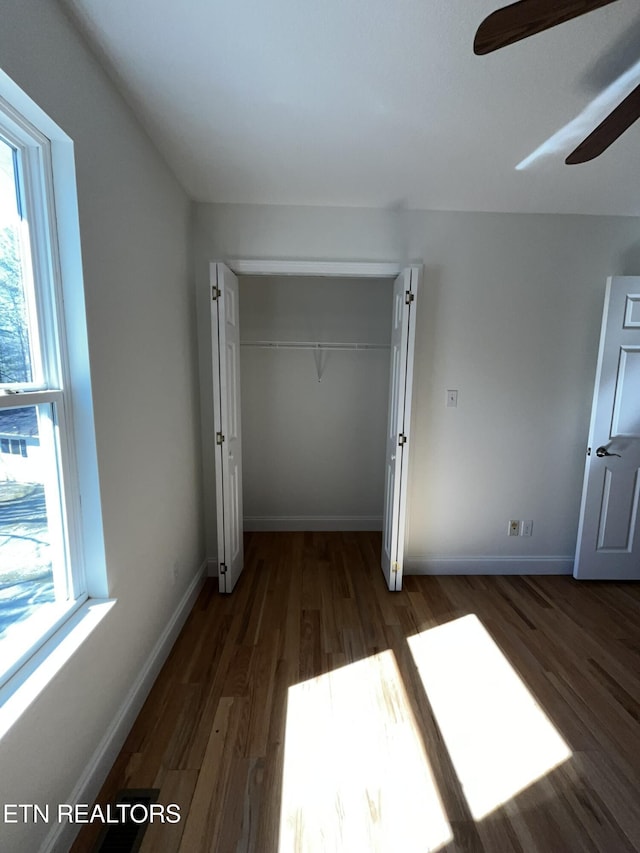 unfurnished bedroom with dark wood-style flooring, a closet, and baseboards