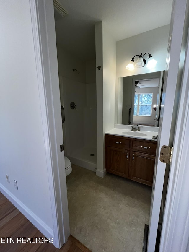 bathroom featuring toilet, a shower stall, baseboards, and vanity