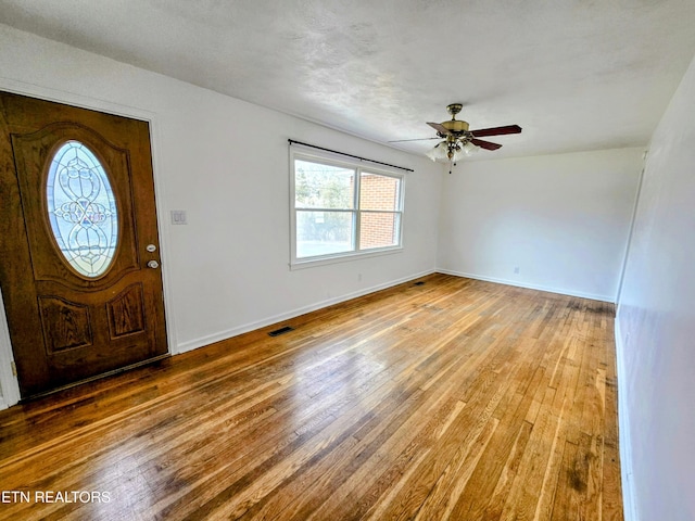 foyer with a ceiling fan, visible vents, baseboards, and wood finished floors