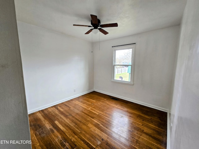 unfurnished room with a ceiling fan, visible vents, dark wood finished floors, and baseboards