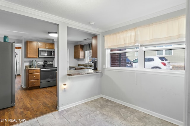 kitchen with baseboards, appliances with stainless steel finishes, brown cabinets, ornamental molding, and a sink