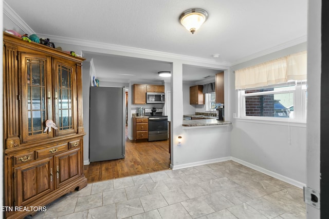 kitchen featuring stainless steel appliances, brown cabinetry, ornamental molding, a textured ceiling, and baseboards