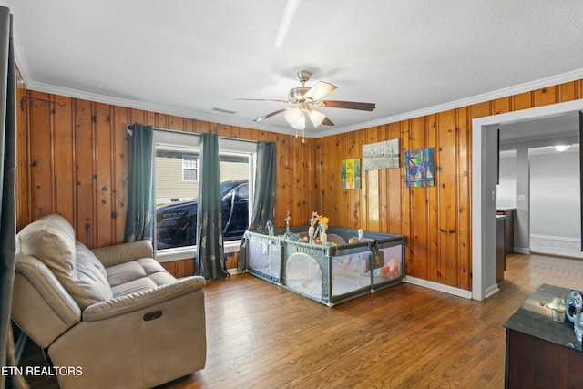 living area with visible vents, a ceiling fan, baseboards, ornamental molding, and dark wood finished floors