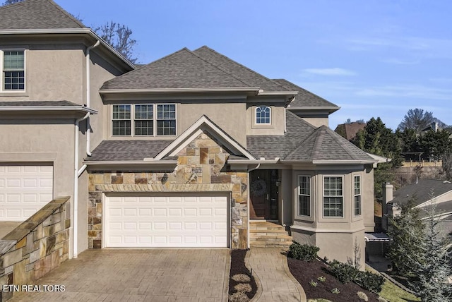 view of front of property featuring an attached garage, stone siding, decorative driveway, roof with shingles, and stucco siding