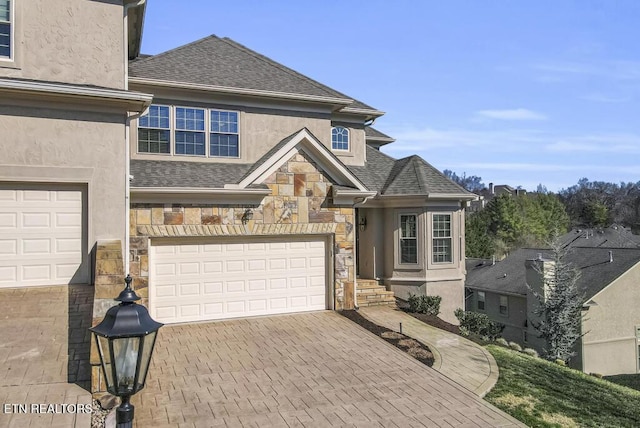 traditional home with stone siding, decorative driveway, roof with shingles, and stucco siding