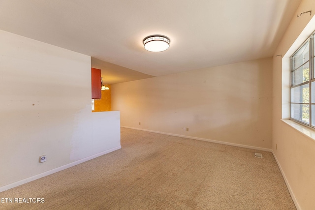 carpeted spare room featuring an inviting chandelier and baseboards