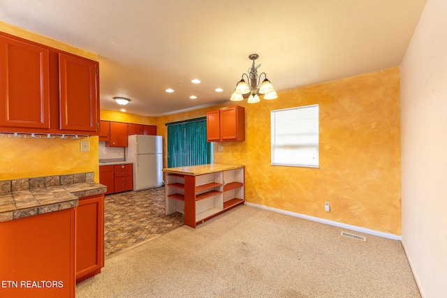 kitchen with tile counters, light colored carpet, decorative light fixtures, freestanding refrigerator, and a notable chandelier