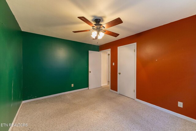 spare room featuring light carpet, ceiling fan, and baseboards