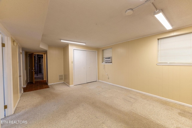 unfurnished room with a textured ceiling, a wall mounted AC, baseboards, and light colored carpet