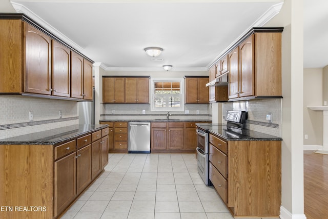 kitchen featuring brown cabinets, light tile patterned floors, stainless steel appliances, a sink, and under cabinet range hood