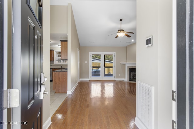 foyer featuring light wood finished floors, a fireplace with flush hearth, visible vents, and baseboards