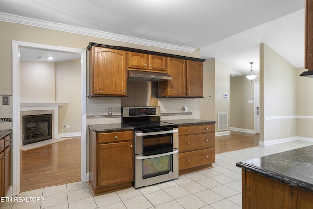 kitchen featuring light tile patterned floors, range with two ovens, brown cabinets, under cabinet range hood, and a fireplace