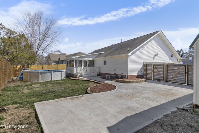 rear view of house with central AC unit, a fenced in pool, a gate, fence, and a yard