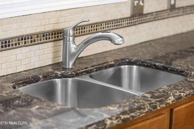 interior details featuring backsplash, dark stone counters, brown cabinetry, and a sink