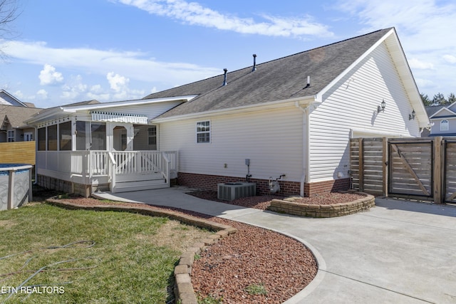 rear view of property with a shingled roof, a lawn, a gate, fence, and central air condition unit